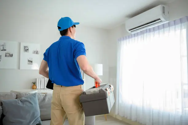 Técnico en uniforme azul llevando caja de herramientas en interior de vivienda — servicio de reparación a domicilio
