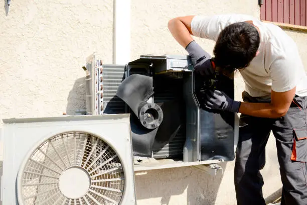 Técnico con herramientas trabajando en la unidad exterior de aire acondicionado — reparación de sistemas de refrigeración